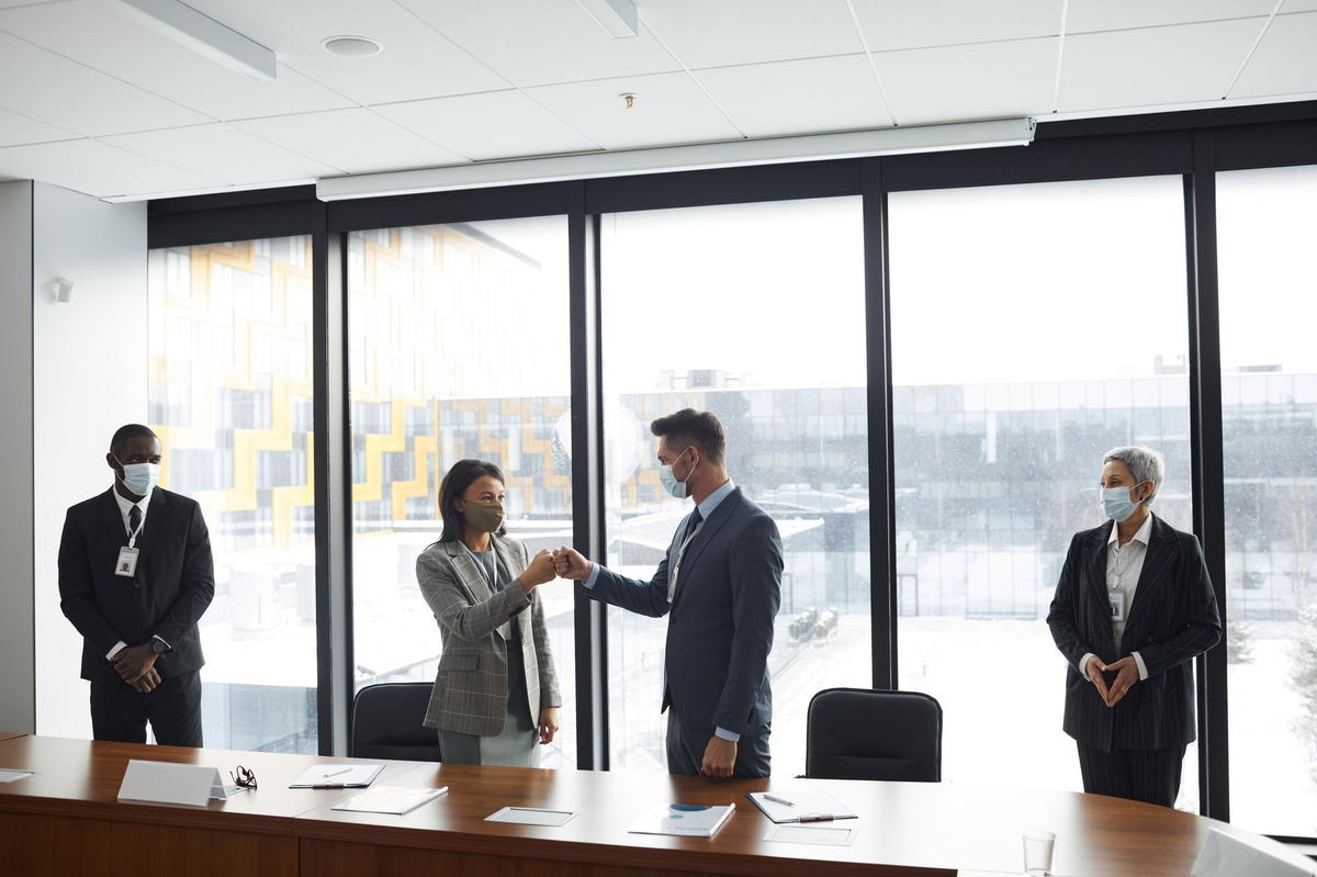 Diverse professionals in formal attire fist bumping at a business meeting in a conference room.