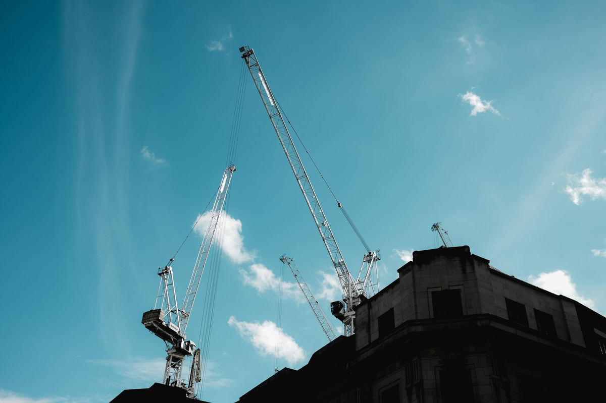 Silhouetted construction cranes extend into a clear blue sky.